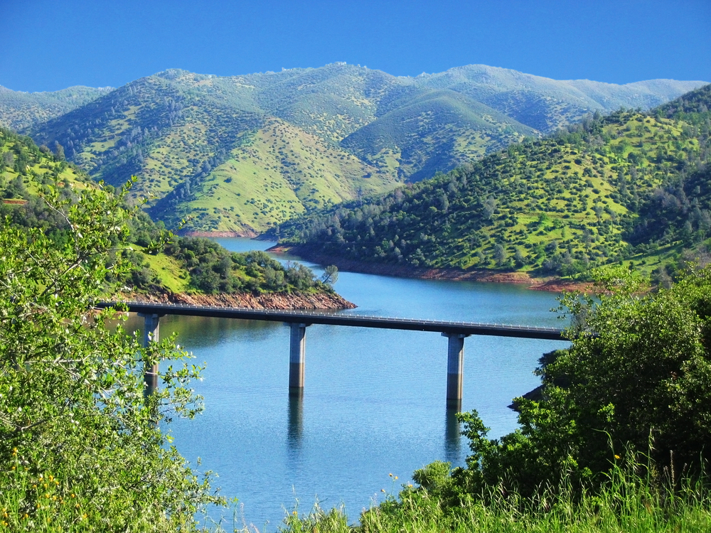 A train rail above a river surrounded by green hills. 