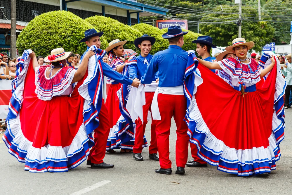 Locals performing a street dance during a festival while wearing vibrant blue and red clothes.