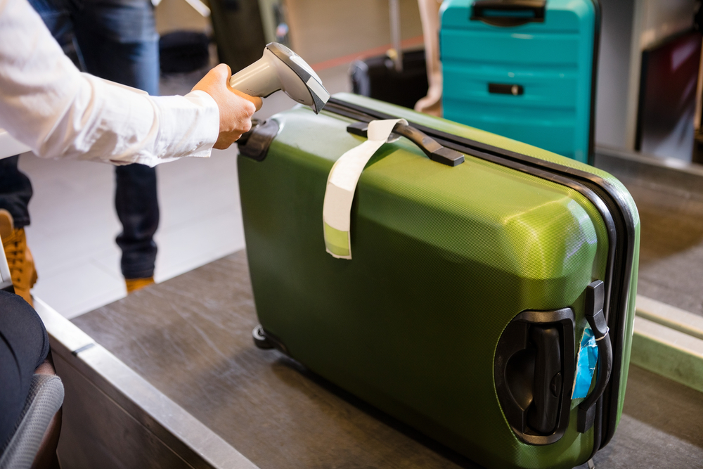 Woman scans green luggage that's been tagged to incur Frontier Airlines baggage fees in the airport before a flight boards