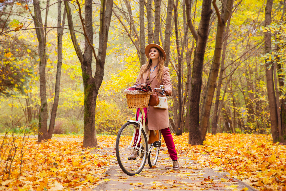 A woman mounted on her bicycle while wearing a coat and a hat during an autumn season. 
