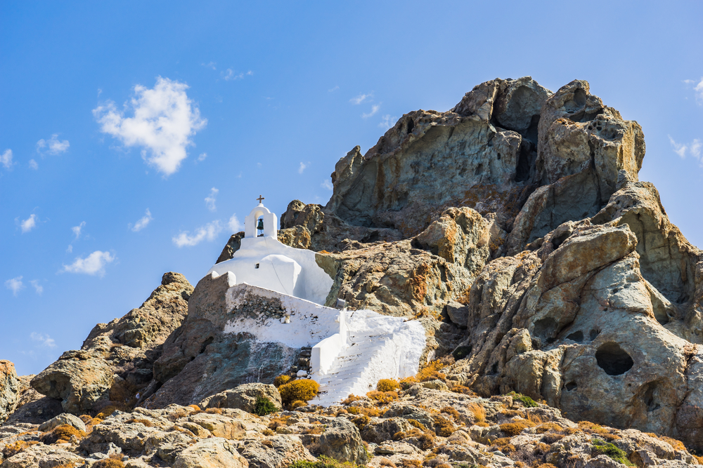 A white chapel that seem to be integrated on the rocks on a mountain.