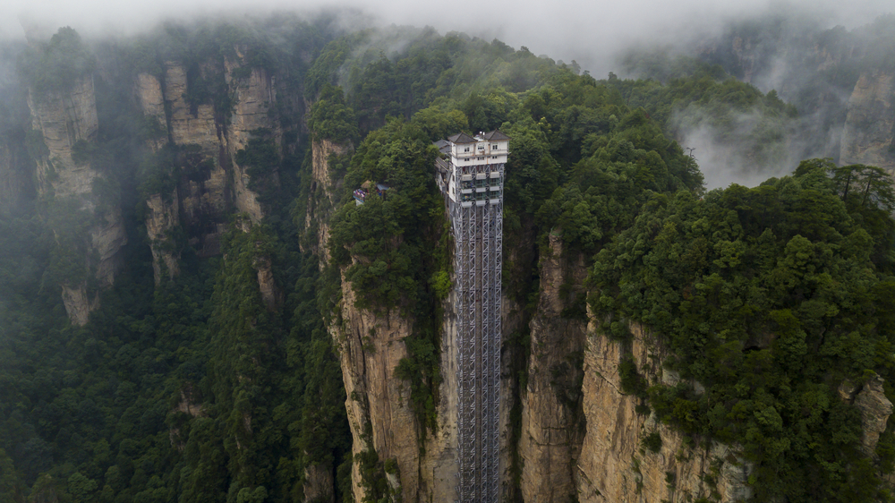 An extremely tall structure built on the side of a cliff from top to bottom.