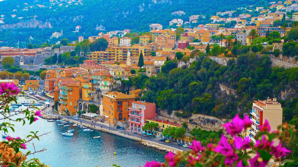 Aerial view on a coastal town in Côte d’Azur, one of our picks on the best areas to stay in France, where boats can be seen moored at the pier, and hotel structures can be seen the coasts and the other part of the town can be seen in background. 