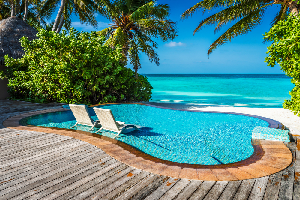 Private beachfront pool with loungers in the water and surrounding palm trees and greenery for a guide showing how long is a flight to the Maldives from the United States with 3 stops