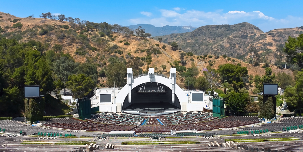 A stage with a half circle structure facing many empty benches and mountains in background.