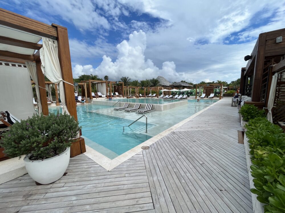 The main pool at the Vidanta Riviera Maya's Beach Club with a pool deck and cabanas surrounding the water