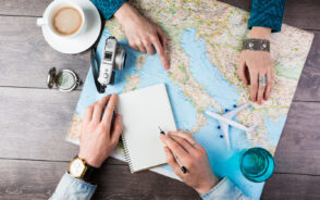 Image looking down at two people's hands on a map of Europe with coffee, notebook, and plane model to indicate planning a Europe itinerary 2 weeks long to sightsee