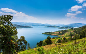 A view from the side of a calm lake, a picture for where to stay in Uganda, where there are other several small islands in the middle and the sides of the lake are surrounded by mountains.