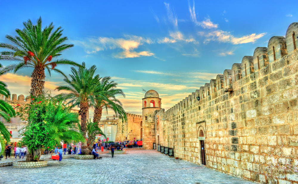 Tall walls made of cobble stones and some palm trees in side a plant circle during sunset. 