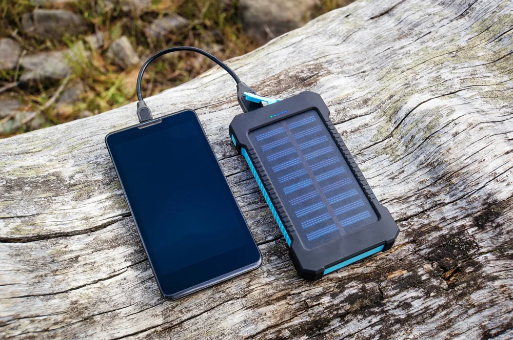 A phone being charged using a solar charger both placed on a log. 