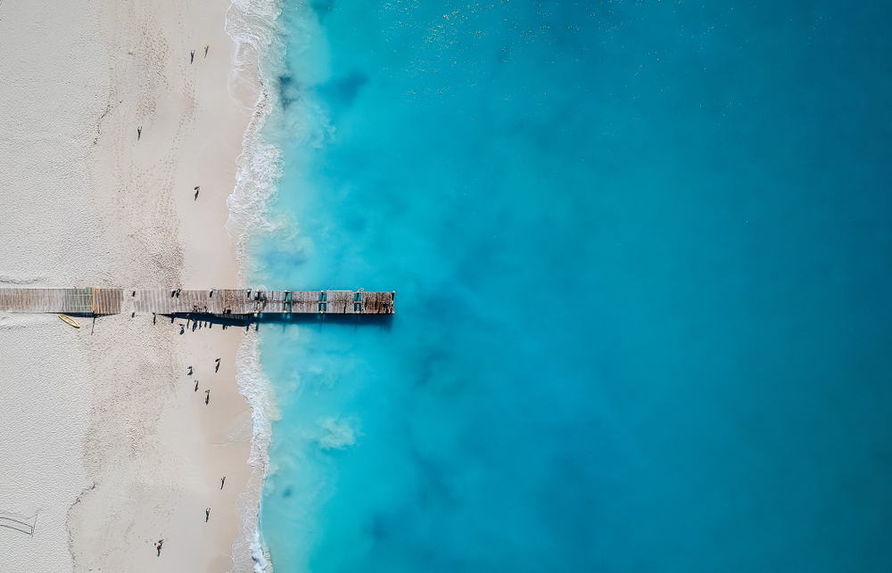 Top view on a beautiful beach with a wooden dock and emerald waters. 