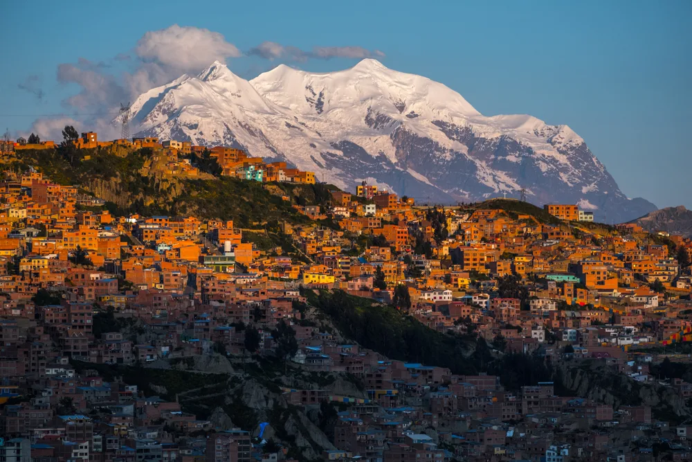 A sunset over a city built on a steep landscape with an icy mountain in background, a city in South America built on high elevation, an image for a guide on the facts about the region.