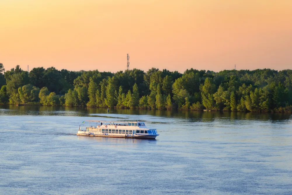A cruise ship sailing on a wide river with lush trees on its banks during sunset, a piece for the guide titled what is in Eastern Europe.