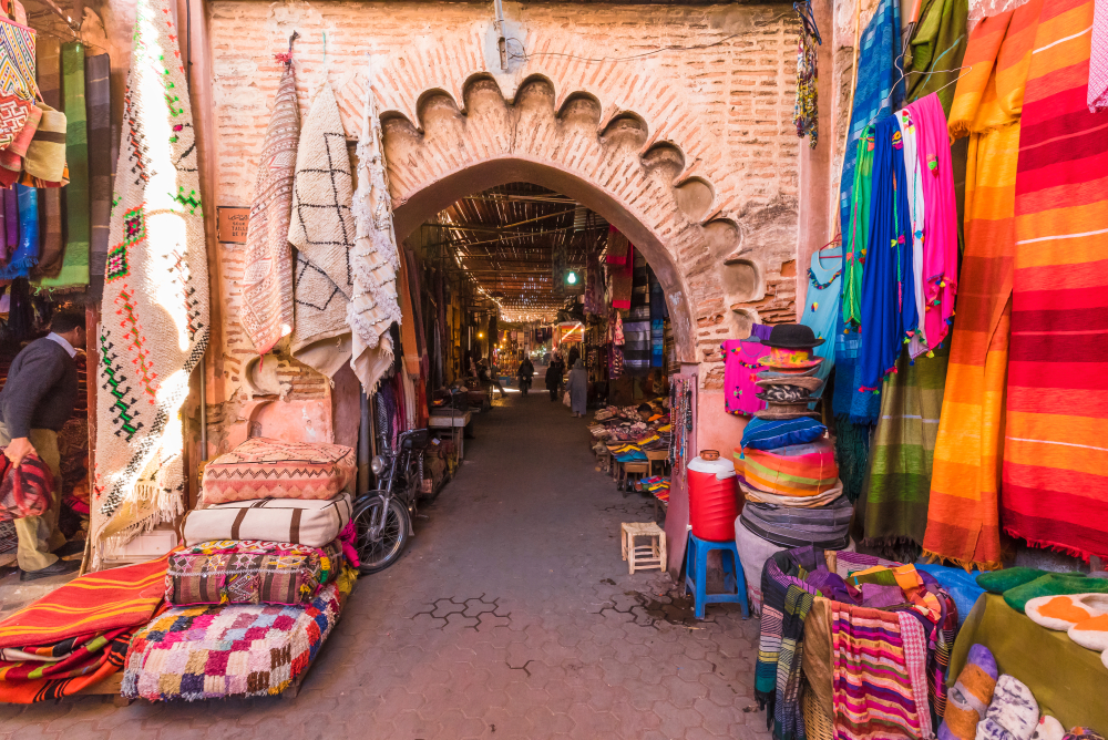 An arched entrance to the market photographed for a piece on where to stay in Marrakech, vibrant colored fabrics are displayed on the walls of the entrance.