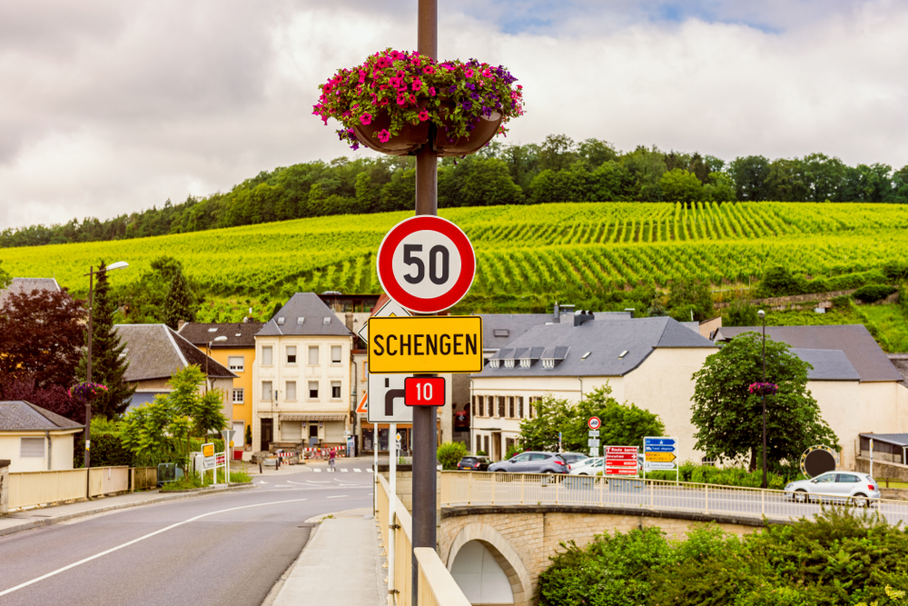 A road sign that says Schengen and in background is a wide vineyard, in a country town in the Eastern Europe.