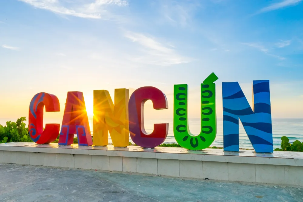 Colorful Cancun letters standing in front of a beach at sunset to indicate the concept of how long is a flight to Cancun from the US