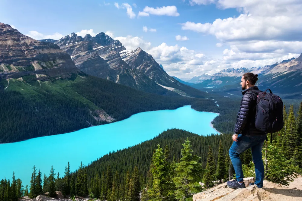 A hiker standing on a rock overlooking the view of a lake at the Banff National Park that is reflecting the sky, an image for a guide about the best time to visit Banff National Park.