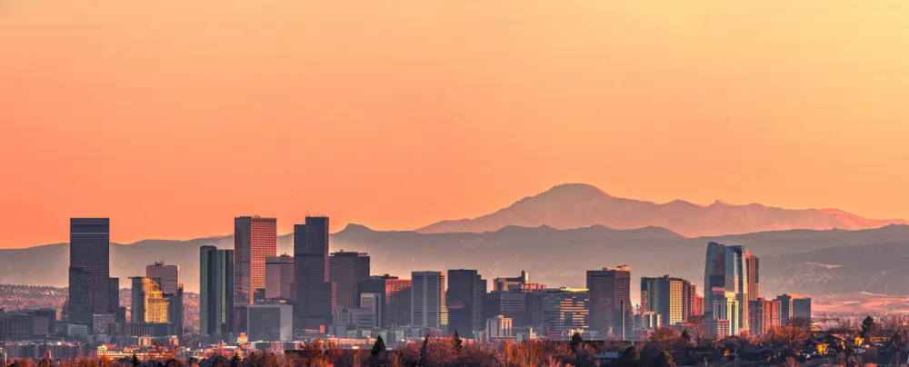 A city skyline during sunset and mountains can be seen in background.