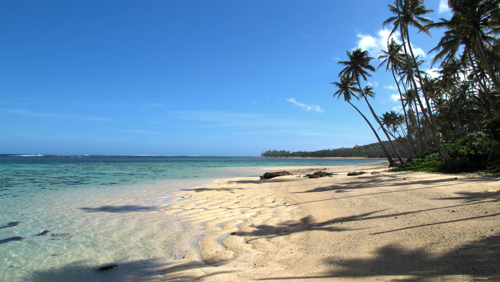 One of the best beaches in Fiji with white sand and palm trees creating shade for a frequently asked questions section on how long is a flight to Fiji