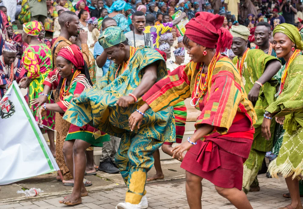 Locals wearing green and red patterned clothes while dancing barefoot on the streets during a festival. 