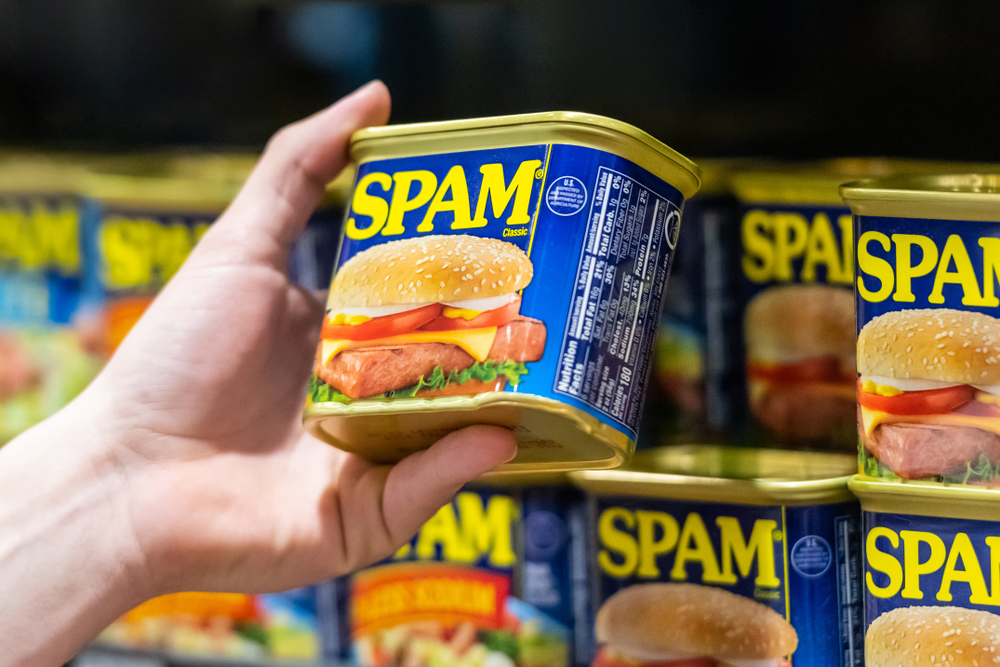 Hand picking up a can of SPAM classic canned meat in the grocery store for a section covering the history of SPAM