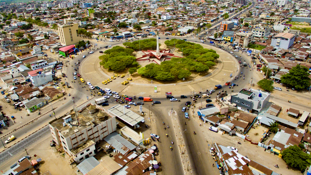 Aerial view on a roundabout in the middle of a city where a garden and a tower can be seen at the center of it. 