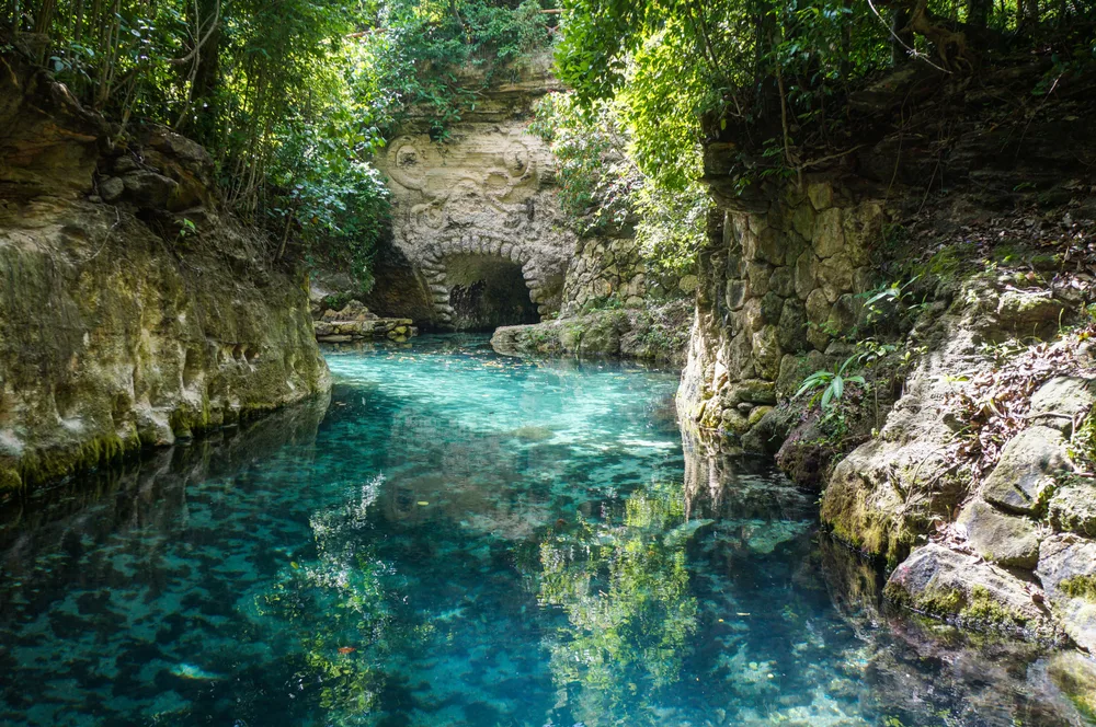 Paradise River in Cancun, Quintana Roo Mexico with dappled sunlight reaching the water and surrounding rocks for a post discussing how long is a flight to Cancun with or without stops