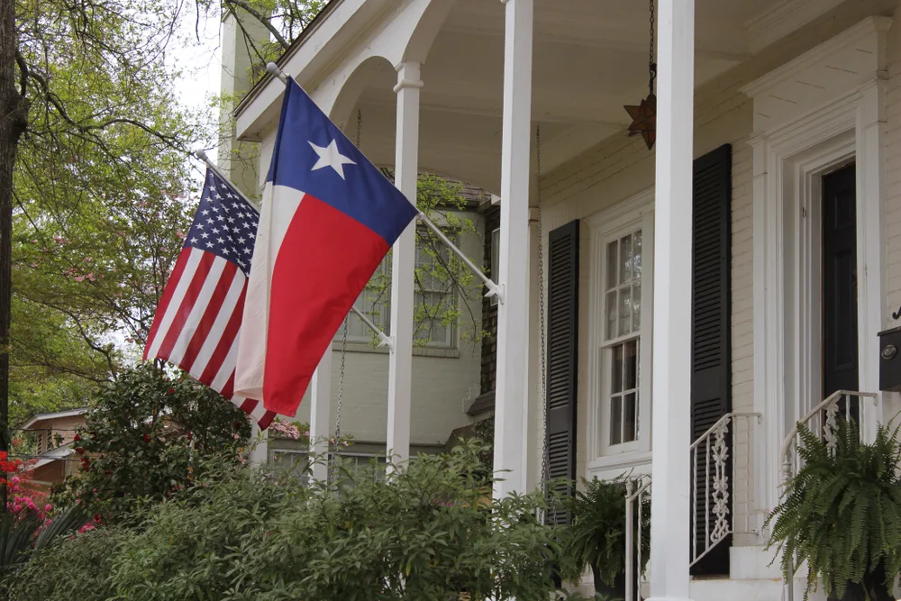 A Texas state flag hanging beside a US flag on a column of an old house. 