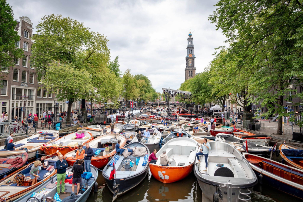 A busy day during the best time to visit Amsterdam at the canal during a festival where it is filled with boats and tourists.