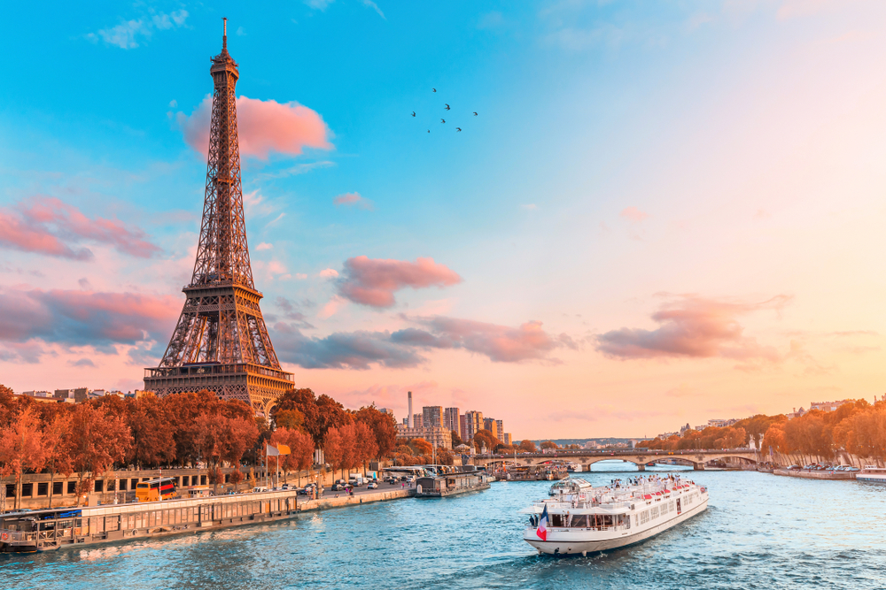 A small cruise ship traversing a river beside the famous Eiffel Tower.