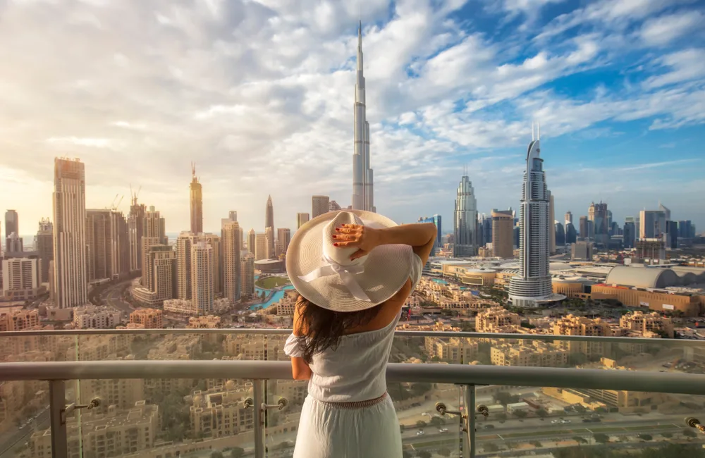 A woman holding her summer hat while looking at a rich city in Dubai filled with tall buildings, captured during the best time to visit the country.