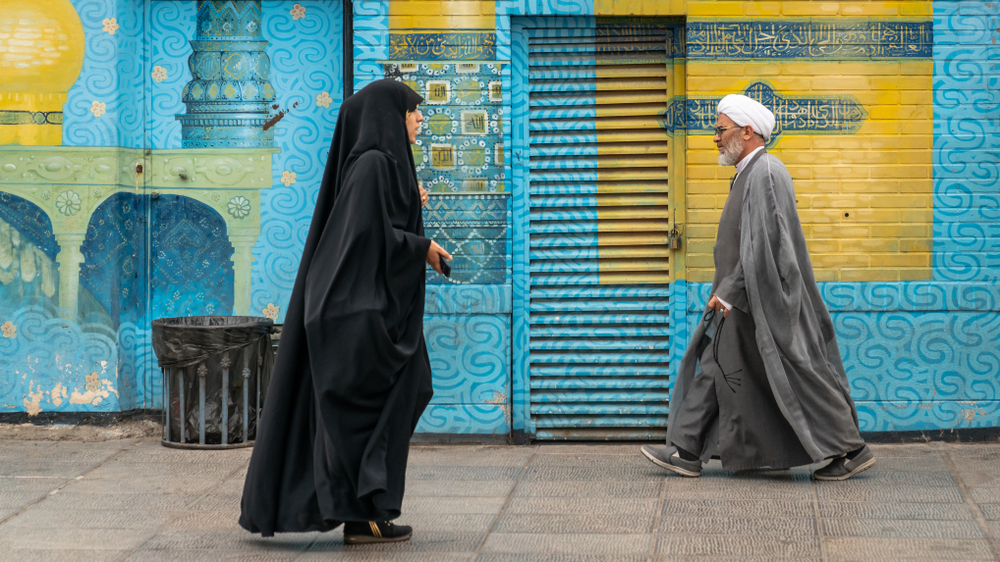 A muslim man and a woman walking on opposite directions in a street. 