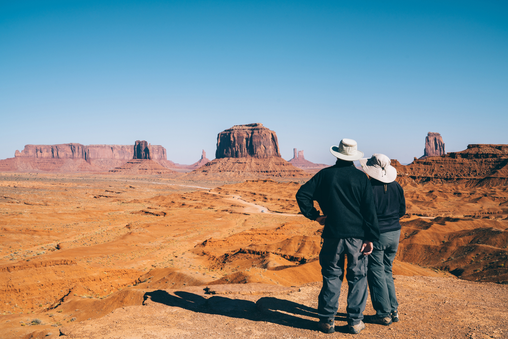 Two people taking a pause from a hiking while looking at a desert landscapes from a distance. 