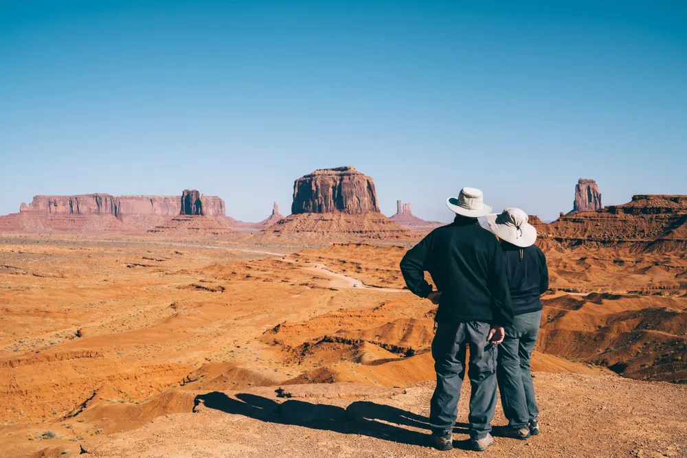 Two people taking a pause from a hiking while looking at a desert landscapes from a distance. 