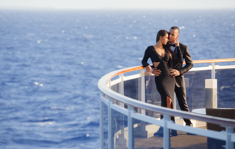 A couple displaying affection on the side of a cruise ship while wearing formal clothes. 