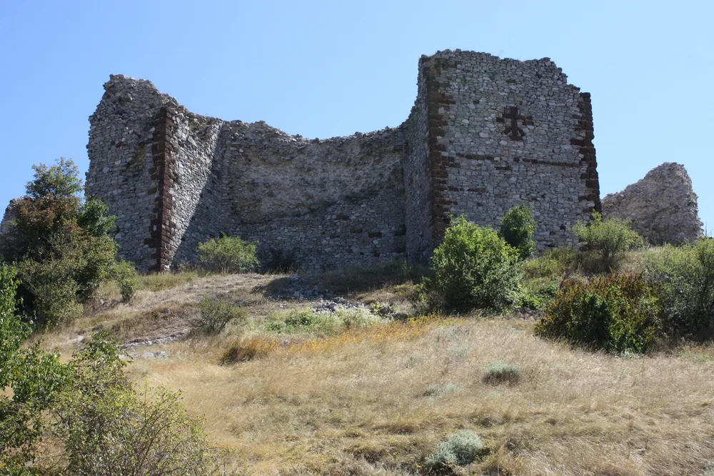 Ruins of a fortress standing on top of a hill with several bushes. 