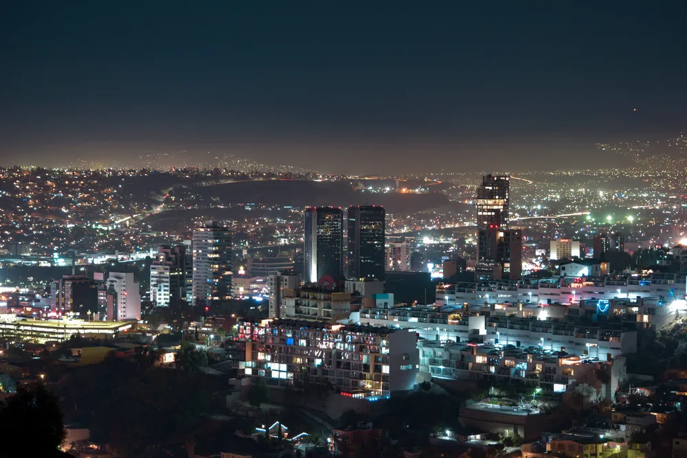 A city at night where silhouettes of buildings are visible through the city lights.