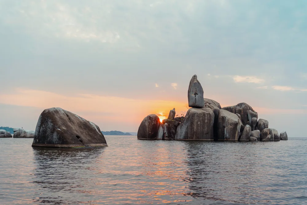 Large rocks can be seen in the middle of the sea during sunset. 
