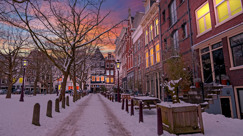 Scenic and snowy winter day in Amsterdam with snow and tire tracks through it with a golden pink sky overhead