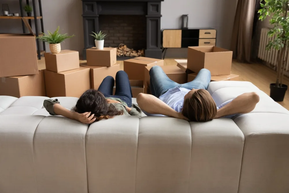 Couple rests on the couch with hands behind their heads before unpacking moving boxes for a guide detailing how to move to Hawaii