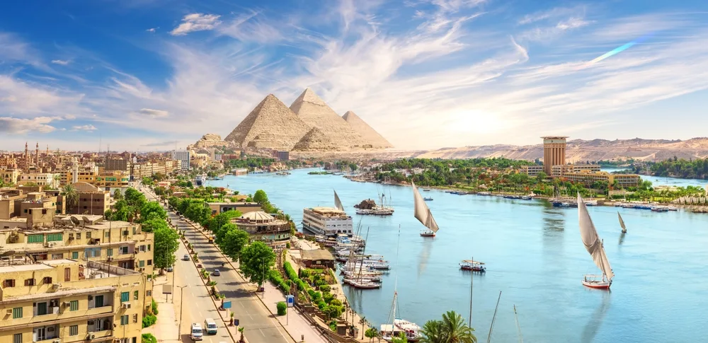The pyramid of Egypt can be seen neat the nile river where boats can be seen traversing the river. 