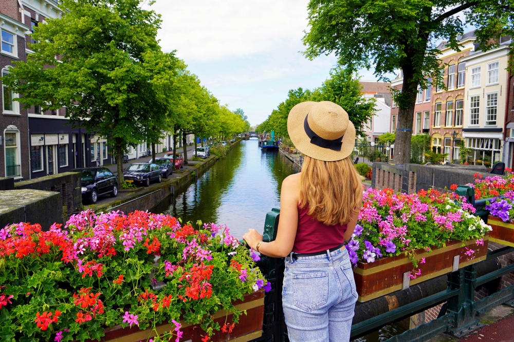 A woman wearing red shirt standing on a small footbridge while looking at the canal during the best time to visit Amsterdam.