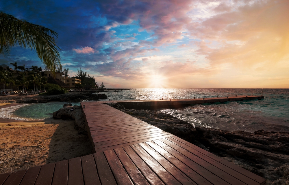 Photo of the sun setting on the picturesque ocean with a wooden dock jetting out into the ocean, an image for the guide about the best time to visit Cozumel.