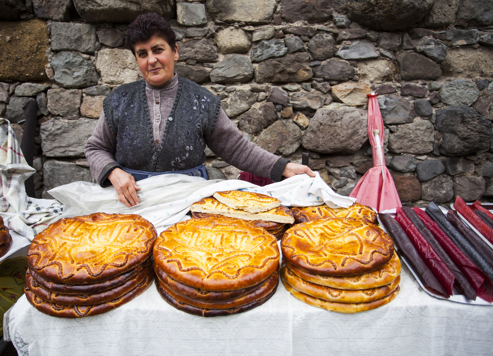 A woman selling piles of circular traditional bread on the side of a street, captured during the best time to visit Armenia.