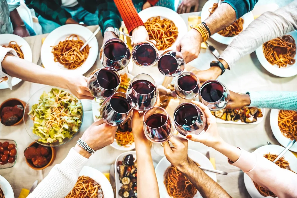 A group of friends raising their wine glasses towards the center for a toast and the food can be seen below. 