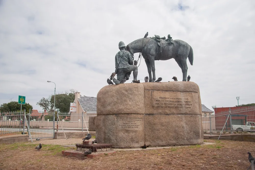 A statue at a park in Gqeberha, one of the best areas to stay in South Africa, where a soldier is kneeling while holding a bucket and feeding a horse.