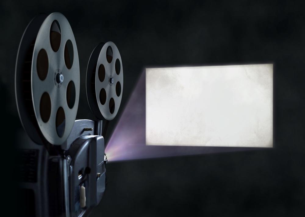An old movie projector emitting light unto a wall. 