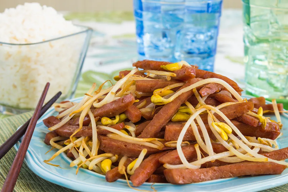 Spam stir fry with bean sprouts placed in front of white rice and a glass of water for a guide detailing why is SPAM so popular in Hawaii