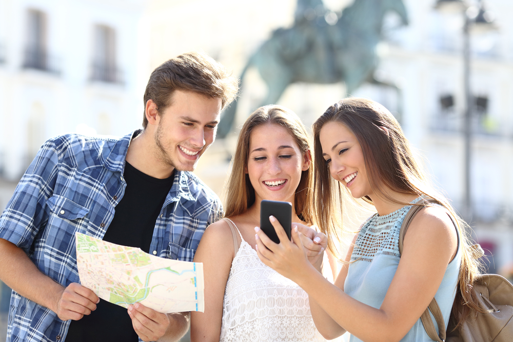 Three people looking at a map and a phone while traveling. 