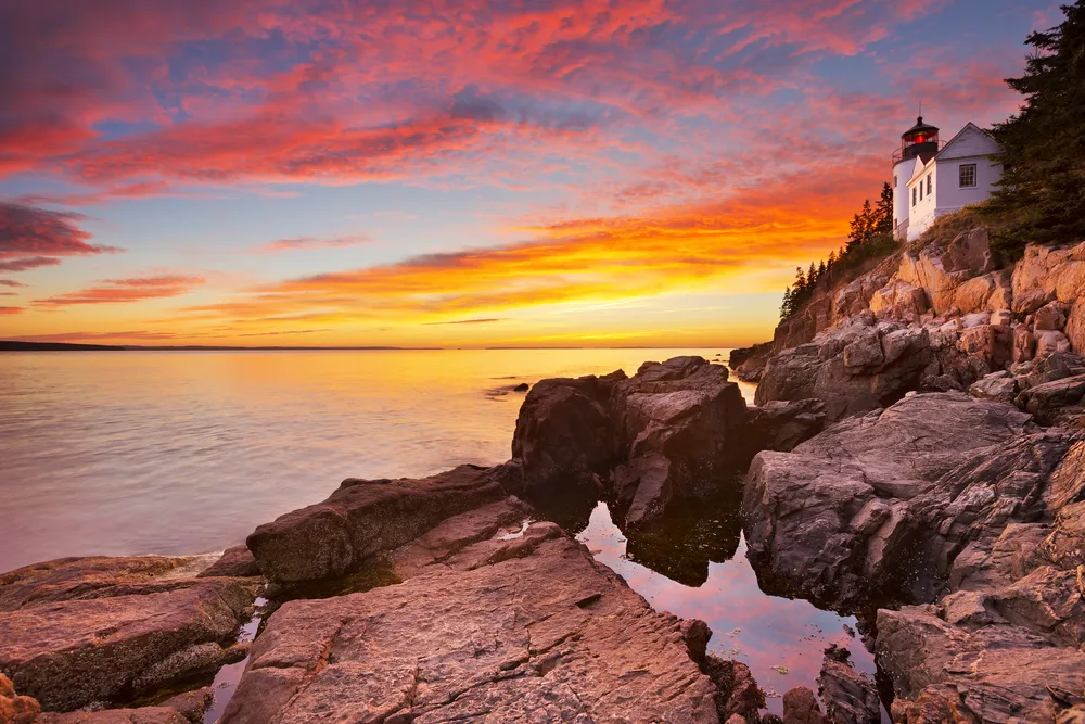 A sunset over a coastal area where a single house can be seen on the rocks, captured during the best time to visit Acadia National Park.